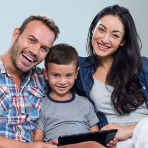 A happy family sitting on a couch, engrossed in a tablet. - Greenberg Legal Group LLC