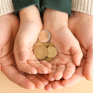 Adult hands cup a child's hands, which hold a small pile of coins, symbolizing financial support or alimony.