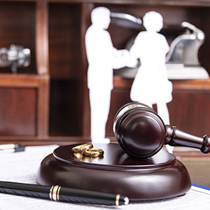 Judge's gavel with wedding rings and paper couple; legal services for marriage and divorce cases.