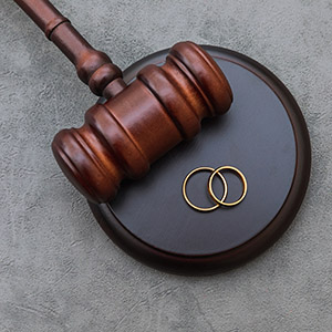 A judge's gavel and two gold wedding rings on a grey surface.